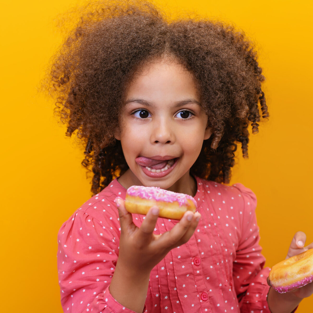 Cravings, sugar cravings, comfort food. Portrait of a happy girl eating donuts. Sugary, sweet foods. Isolated yellow background.