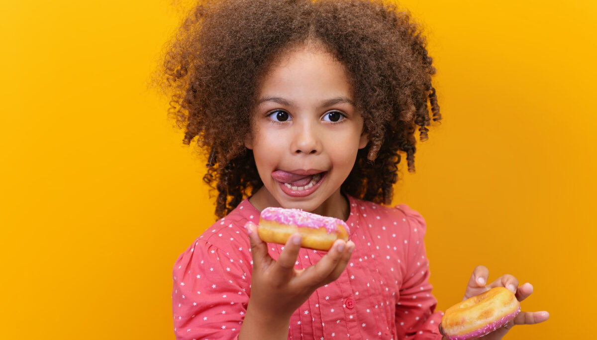Cravings, sugar cravings, comfort food. Portrait of a happy girl eating donuts. Sugary, sweet foods. Isolated yellow background.