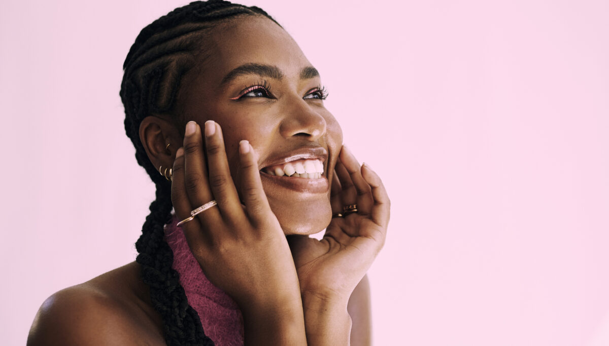 Collagen, summer skin, a close up shot of a beautiful young black woman smiling in front of a pink backdrop