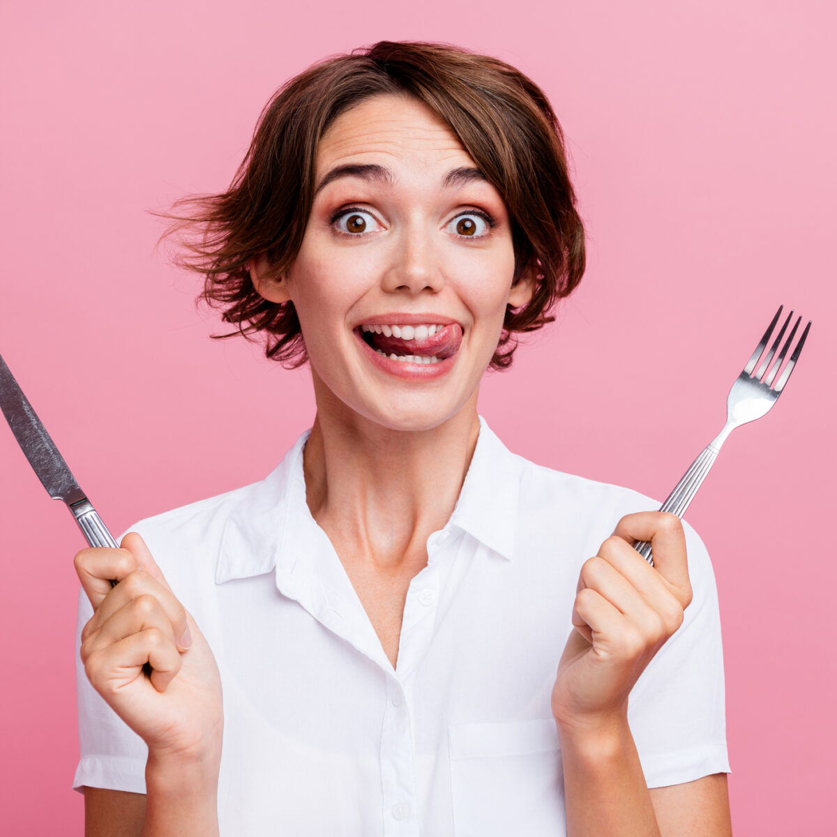 snacks, gut-friendly snacks, Photo of pretty girl licks her teeth she is hungry waiting eating using fork and knife isolated on pink color background.