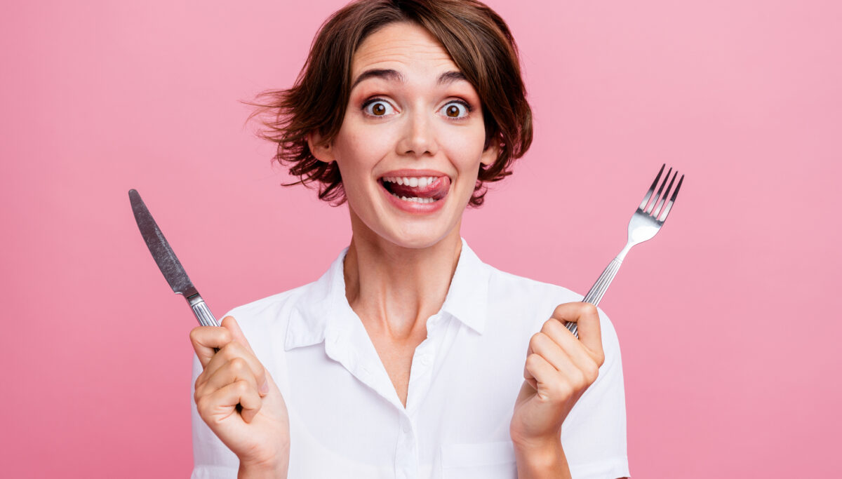 snacks, gut-friendly snacks, Photo of pretty girl licks her teeth she is hungry waiting eating using fork and knife isolated on pink color background.